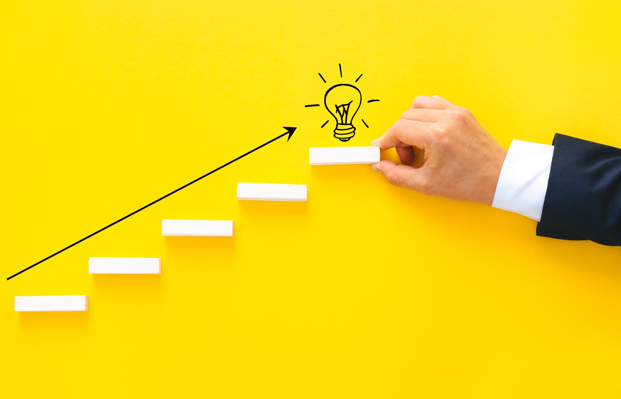 Businessman hand arranging wood block stacking as step stair with lightbulb. Business start-up goals